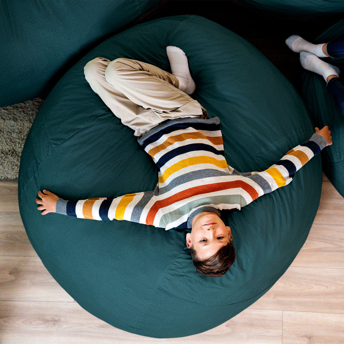 Child lying on a teal bean bag chair with striped sweater