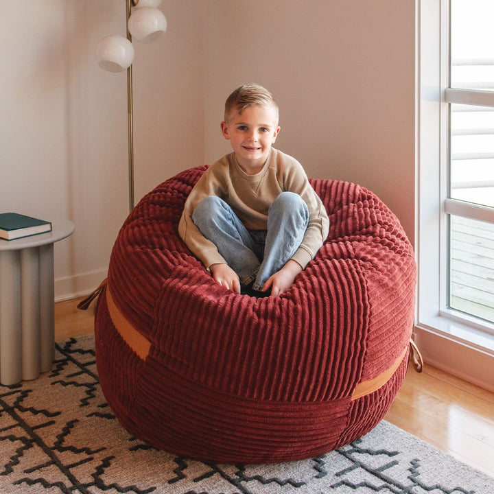 Kid relaxing on a bean bag chair #color_deep-terracotta-corded-plush
