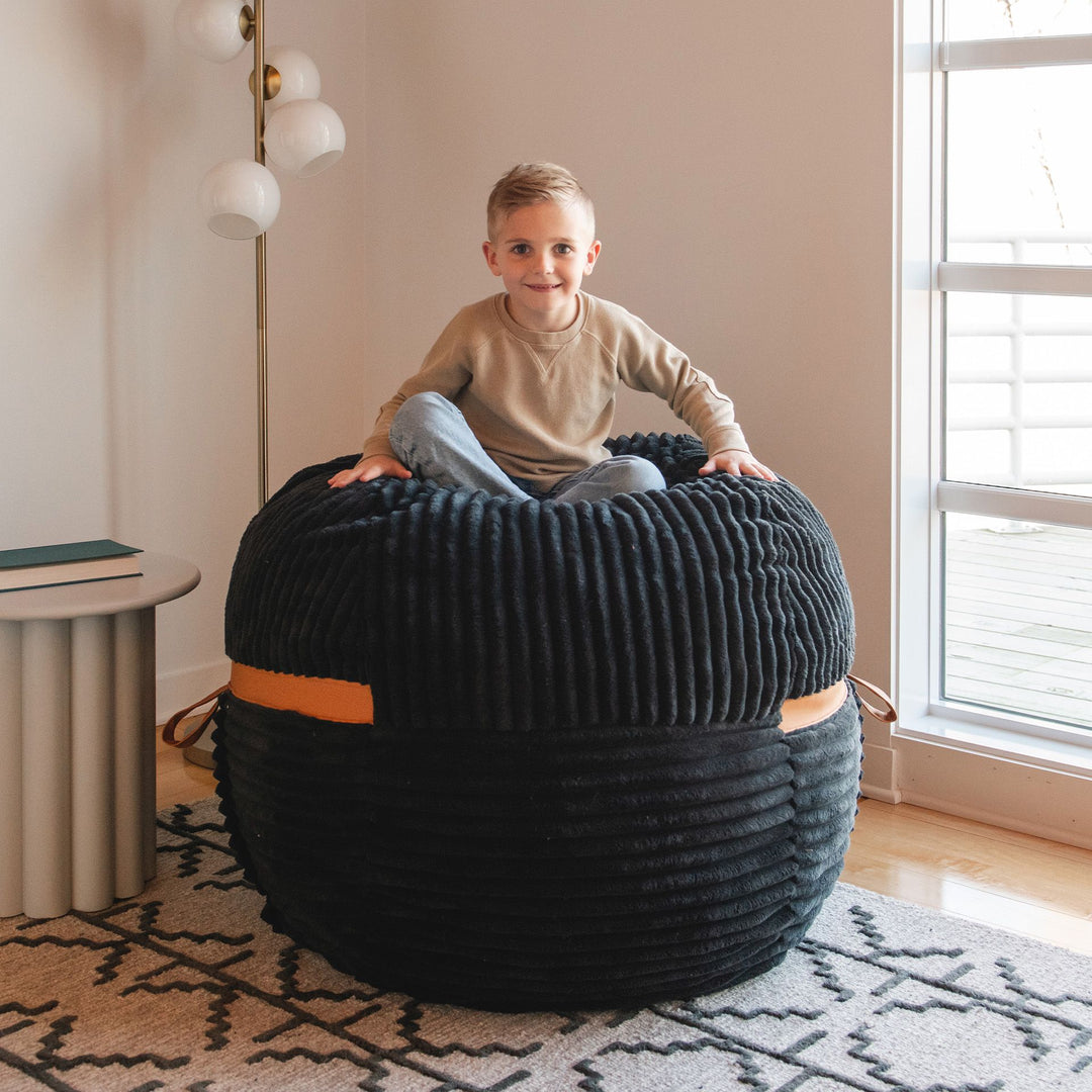 Kid sitting atop a foam bean bag chair #color_black-licorice-corded-plush