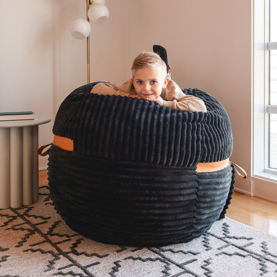 Kid laying on medium kids bean bag chair #color_black-licorice-corded-plush