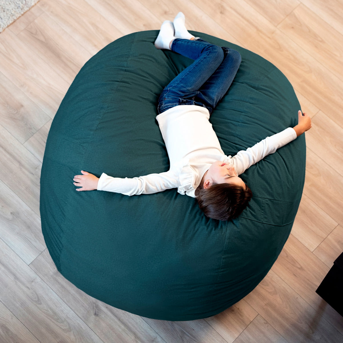 Person lying on a large green bean bag chair on a wooden floor