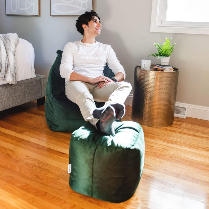 Green velvet Aurora bean bag chair and ottoman combo man relaxing #color_deep-emerald-velvet