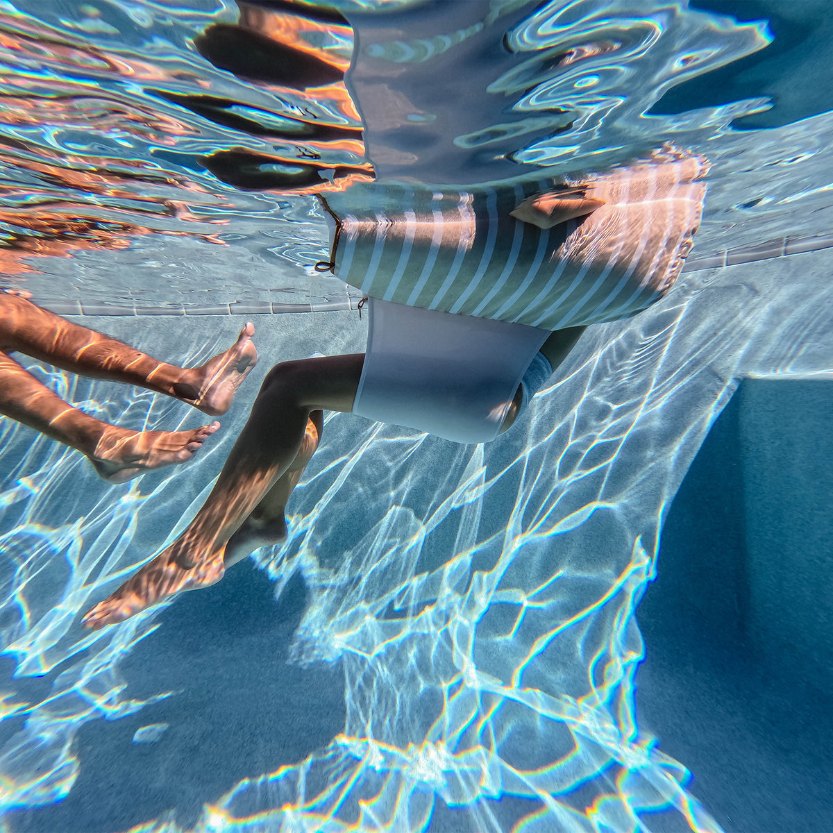 Person floating underwater with clear blue water on a sling chair float