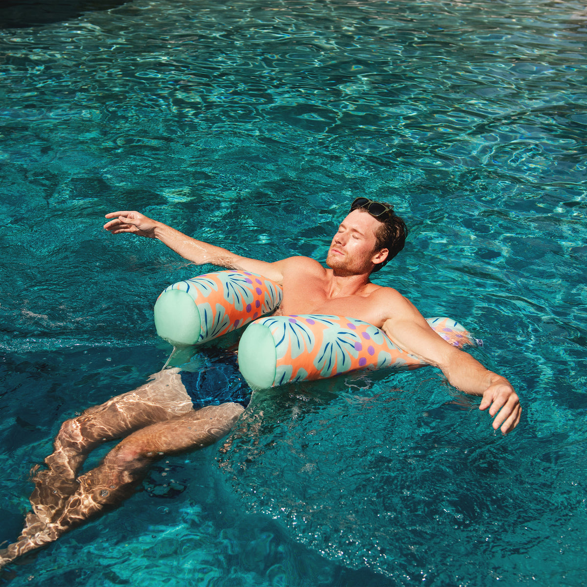 Man floating in a pool with a colorful pool chair