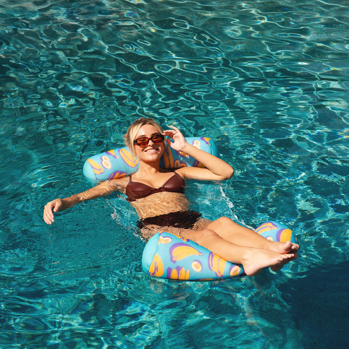 Woman relaxing on a colorful water hammock in clear blue water