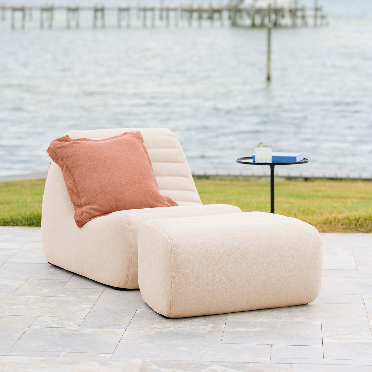 Beige outdoor chair with a pink pillow on a patio near a body of water.