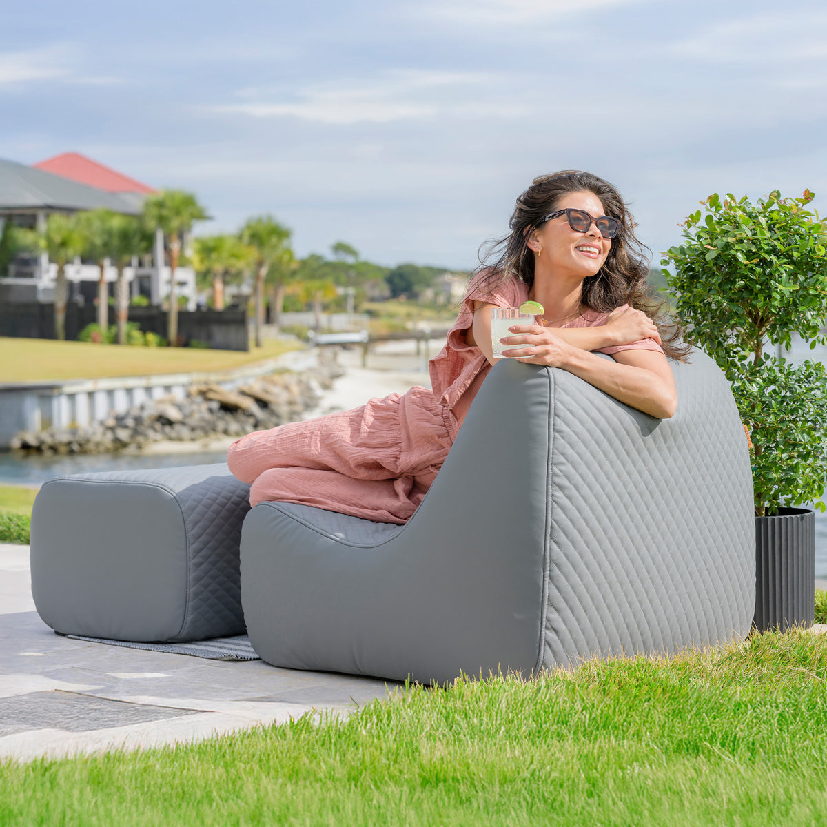 Woman sitting on a gray outdoor patio chair by a waterfront.