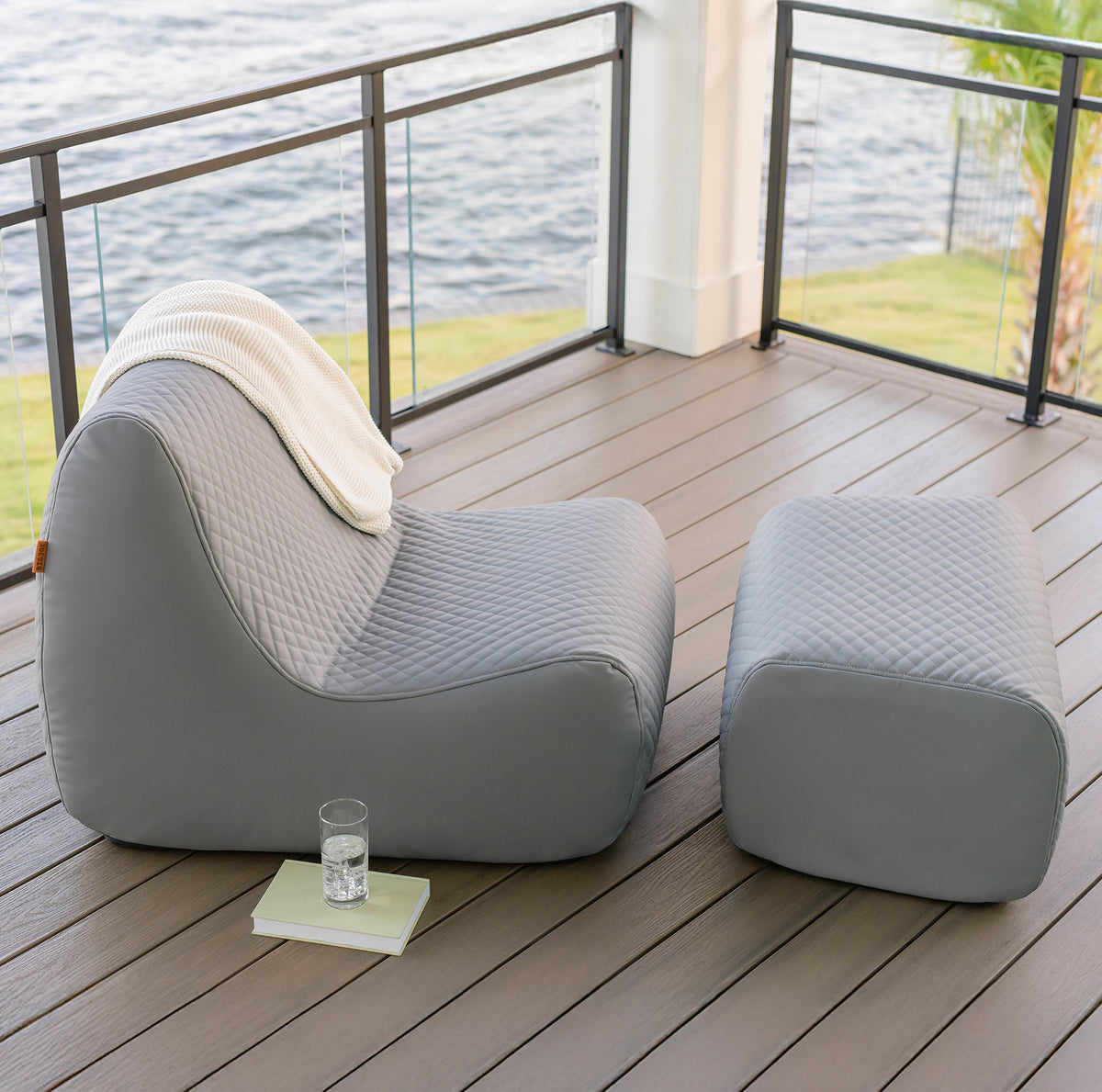 Gray outdoor chair and ottoman on a wooden deck with water view