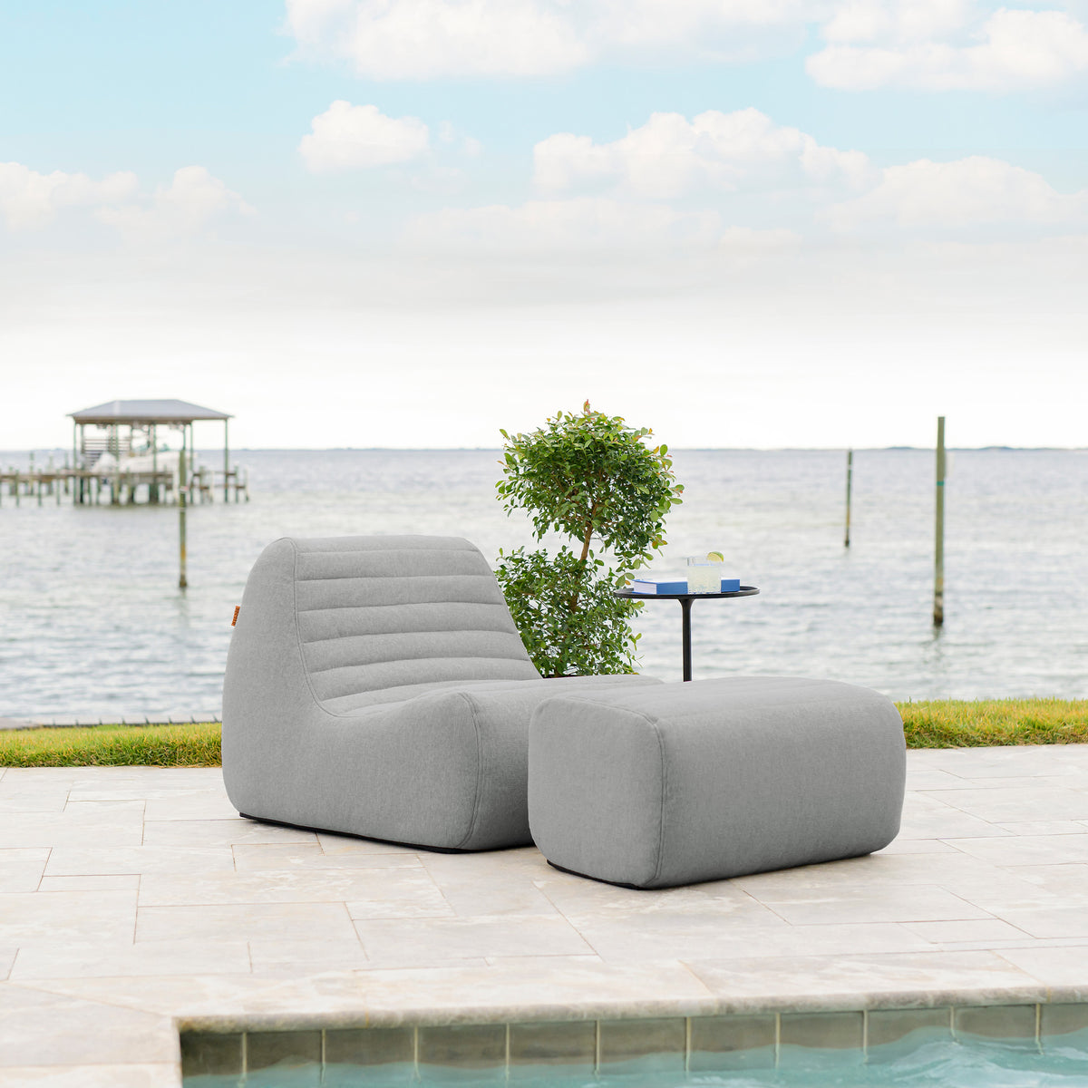 Gray outdoor lounge chair by a pool with water and sky in the background