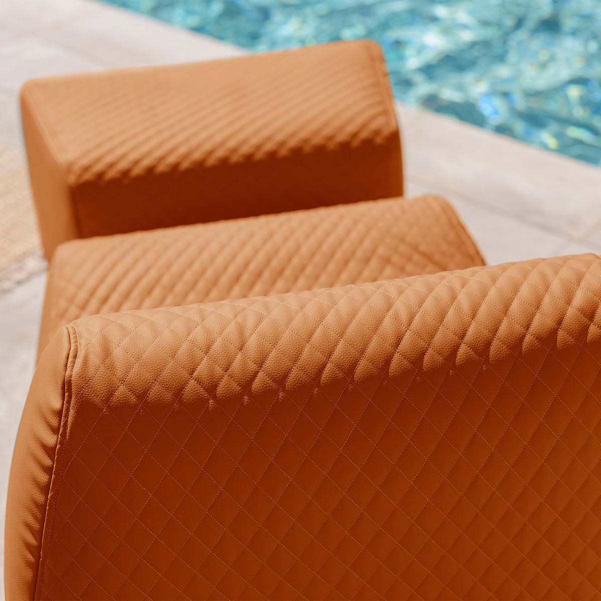 Brown quilted cushions on a white surface near a pool