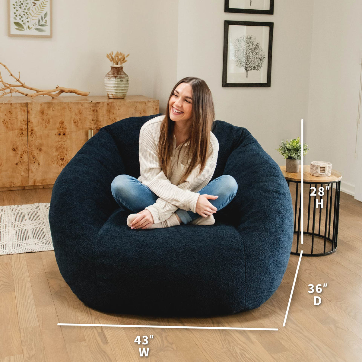 Woman sitting on a navy bean bag chair with dimensions displayed, in a home setting.