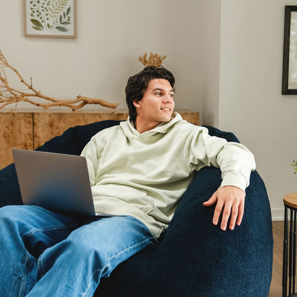 Man working on a computer and relaxing in a blue cloud-like chair in the living room