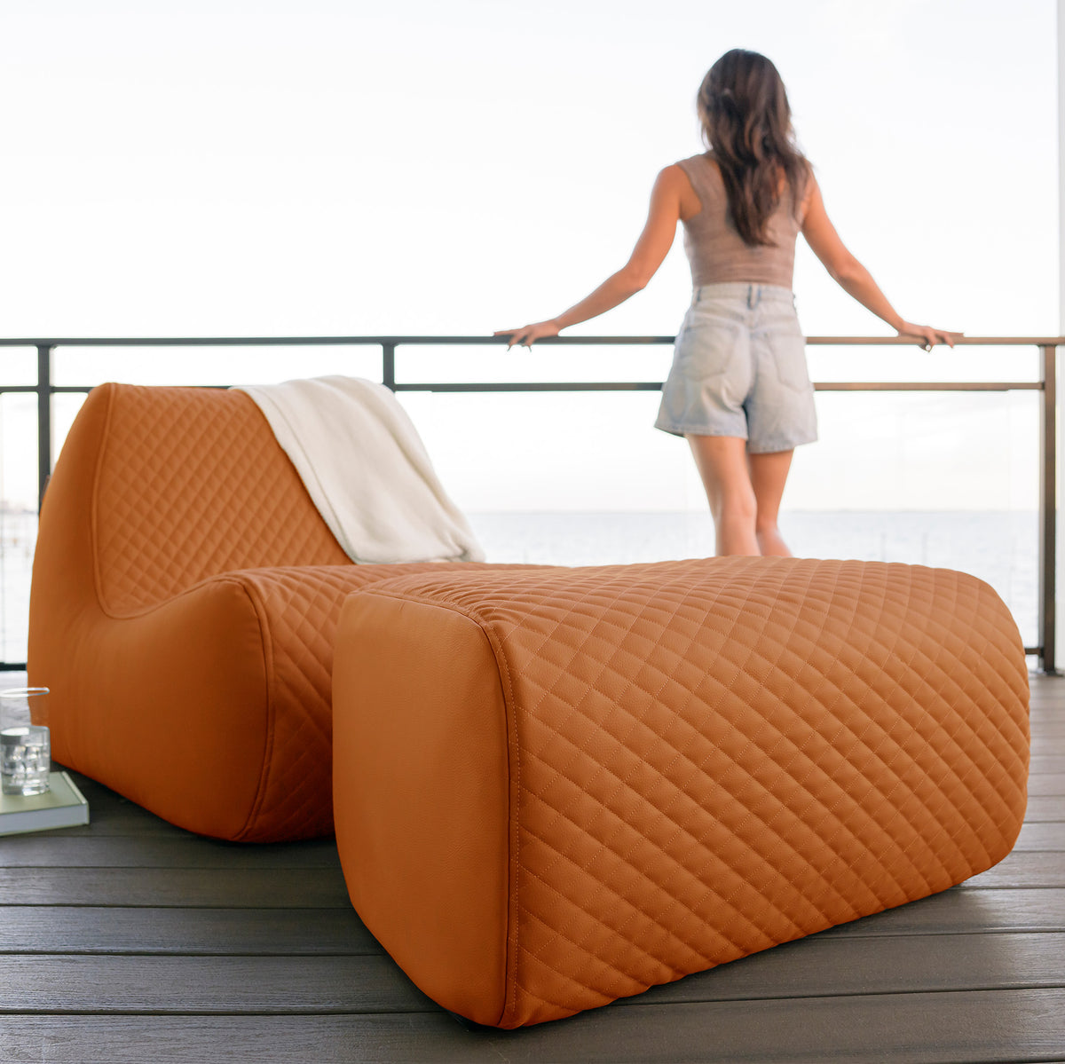 Orange quilted chair on a wooden deck with a woman standing nearby.