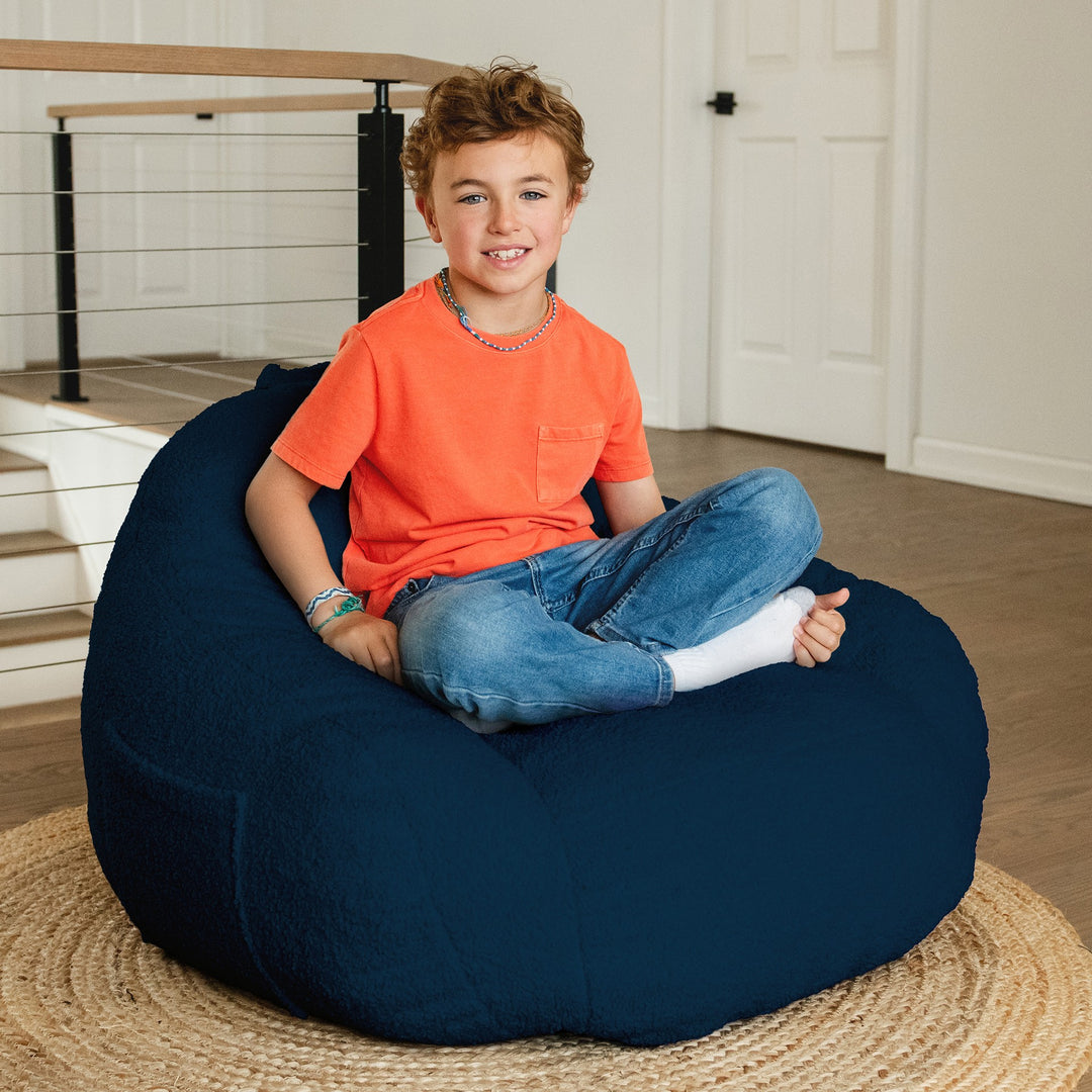 Child sitting on a navy bean bag chair indoors #color_deep-blue-teddy-boucle