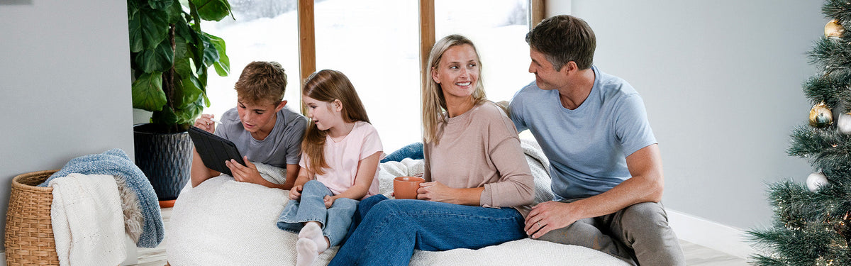 Family sitting on bean bag chair in holiday setting with tree and snow out the back window