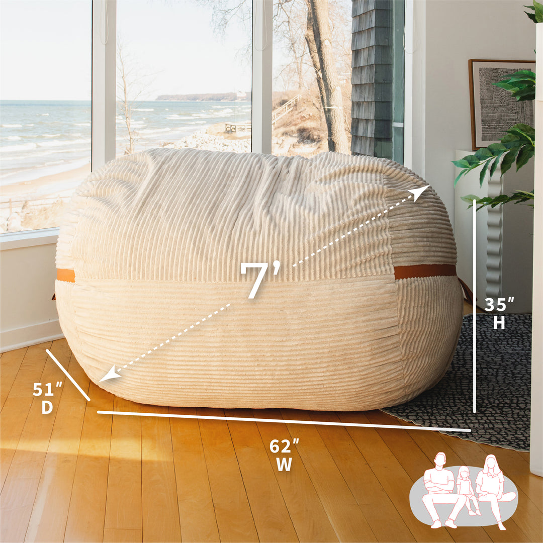 Beige bean bag chair with dimensions labeled in a room with large windows. #color_vanilla-latte-corded-plush