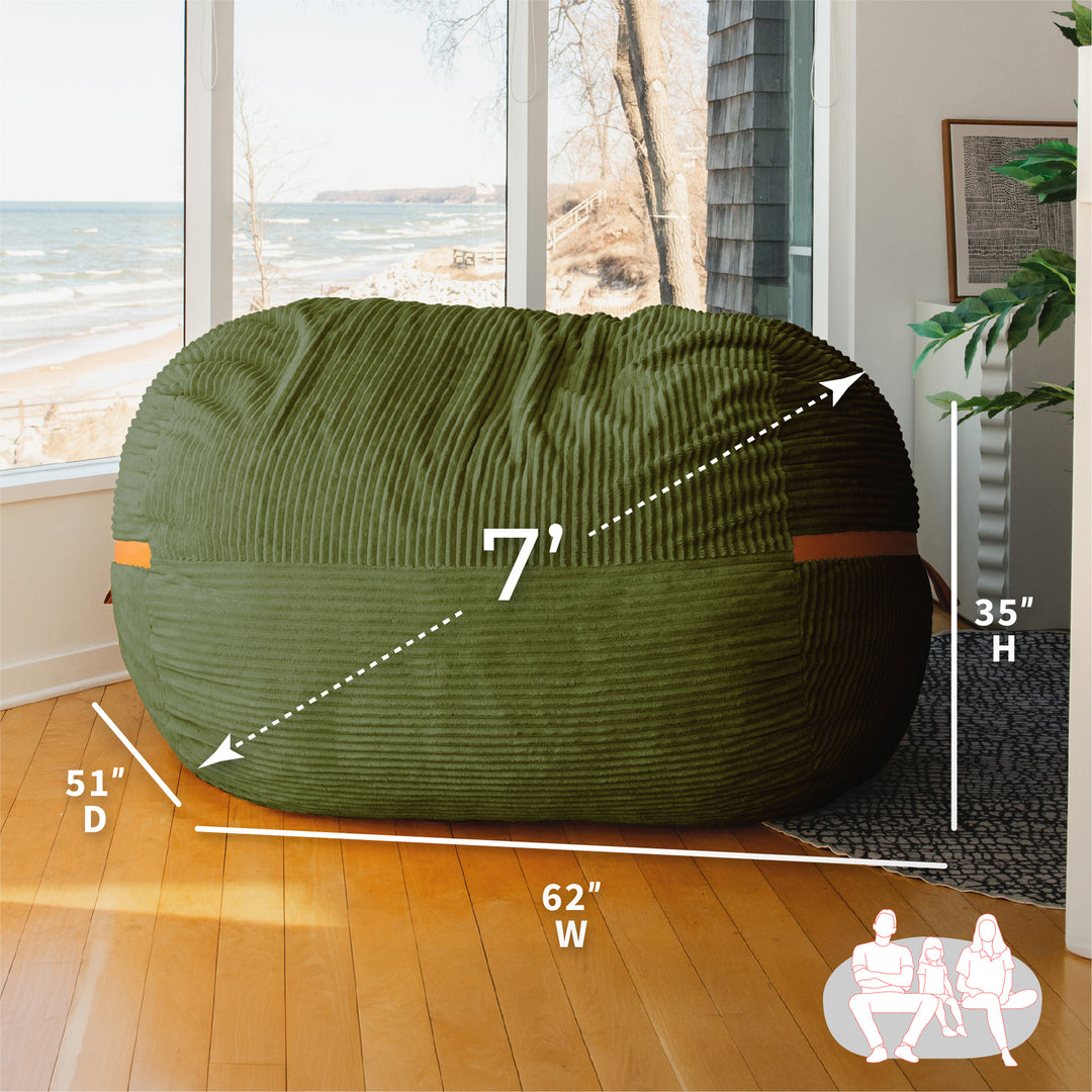 Green bean bag chair with dimensions labeled in a room with large windows. #color_moss-green-corded-plush
