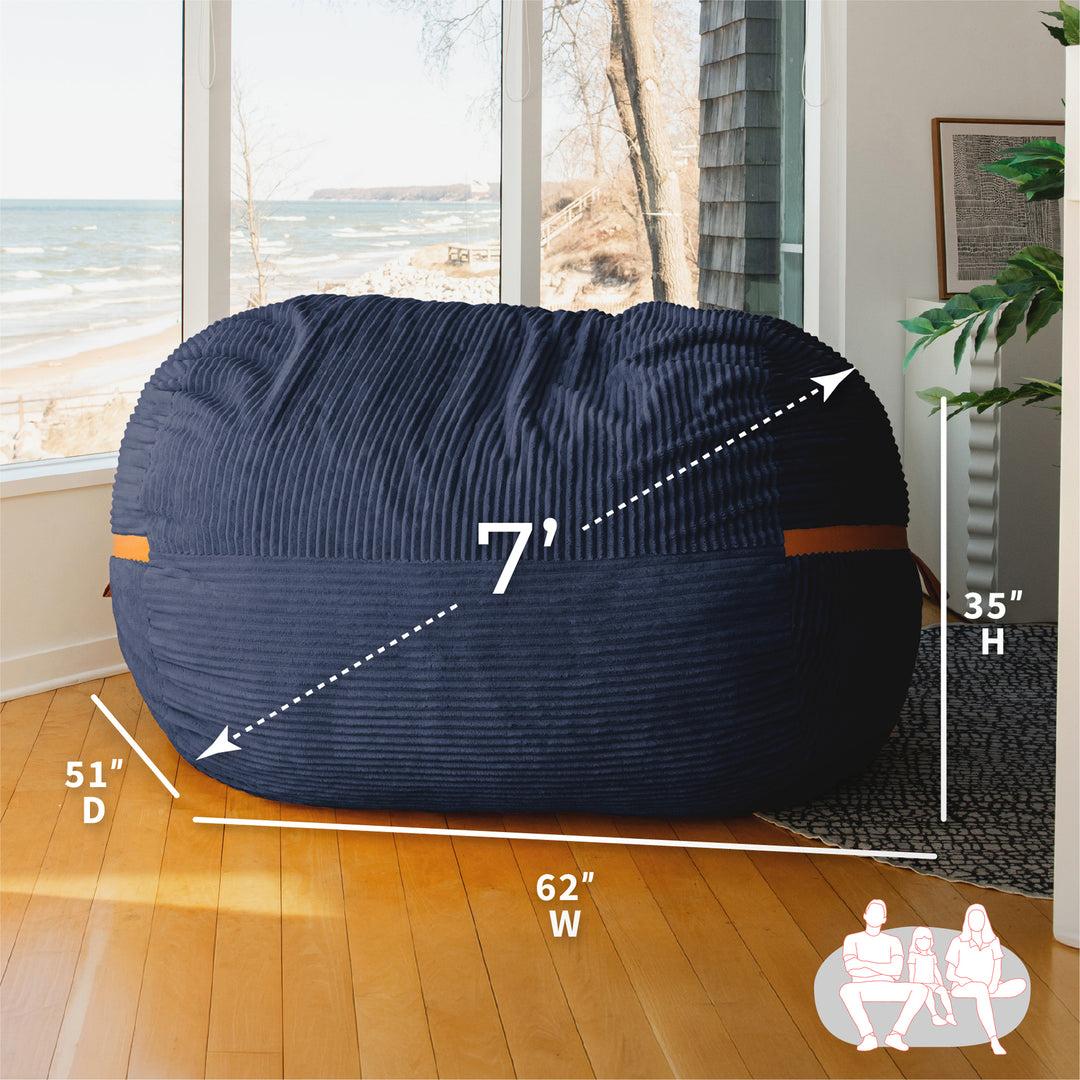 Navy bean bag chair with measurements in a room with large windows. #color_midnight-blue-corded-plush