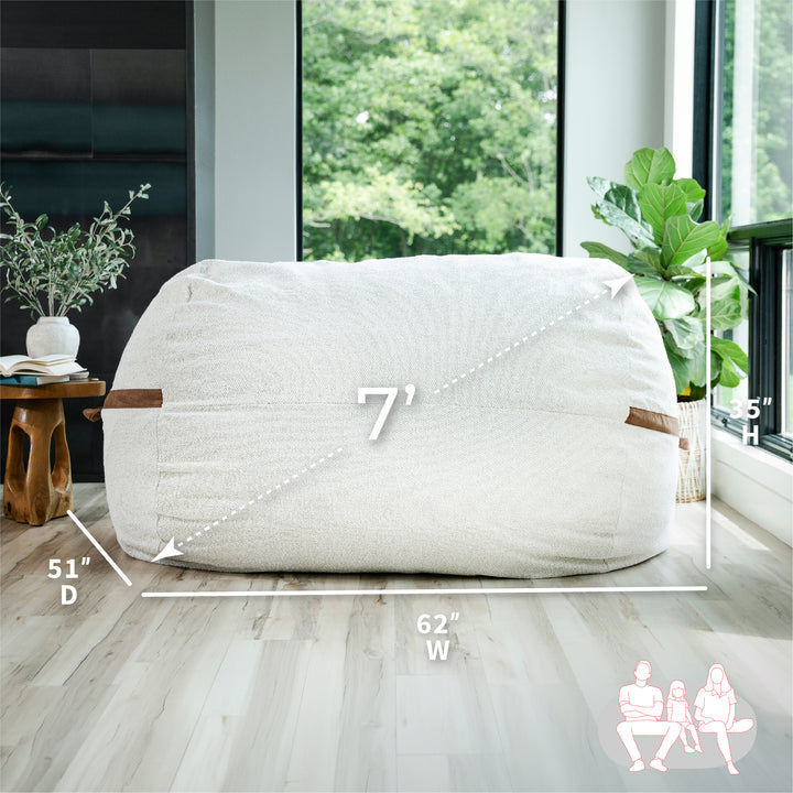 White bean bag chair with dimensions labeled in a room with large windows and plants. #color_sandstone-textured-boucle
