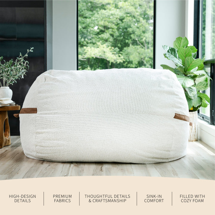 White bean bag chair with wooden handles in a room with large windows and plants. #color_sandstone-textured-boucle