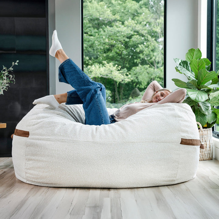 Person relaxing on a large bean bag chair in a modern living room. #color_sandstone-textured-boucle