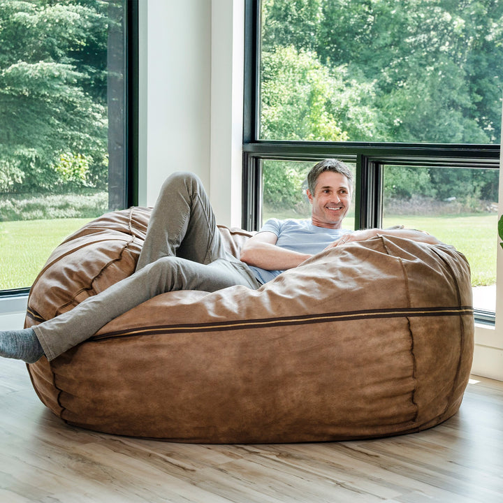 Man relaxing on a large brown bean bag chair in a room with large windows. #color_coffee-soft-vegan-leather
