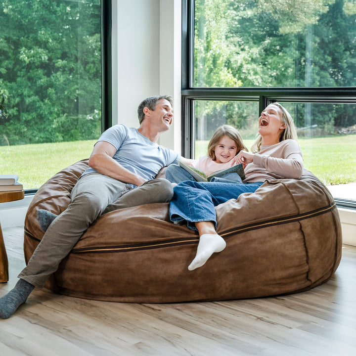 Family of three sitting on a large brown bean bag in a bright room with large windows. #color_coffee-soft-vegan-leather