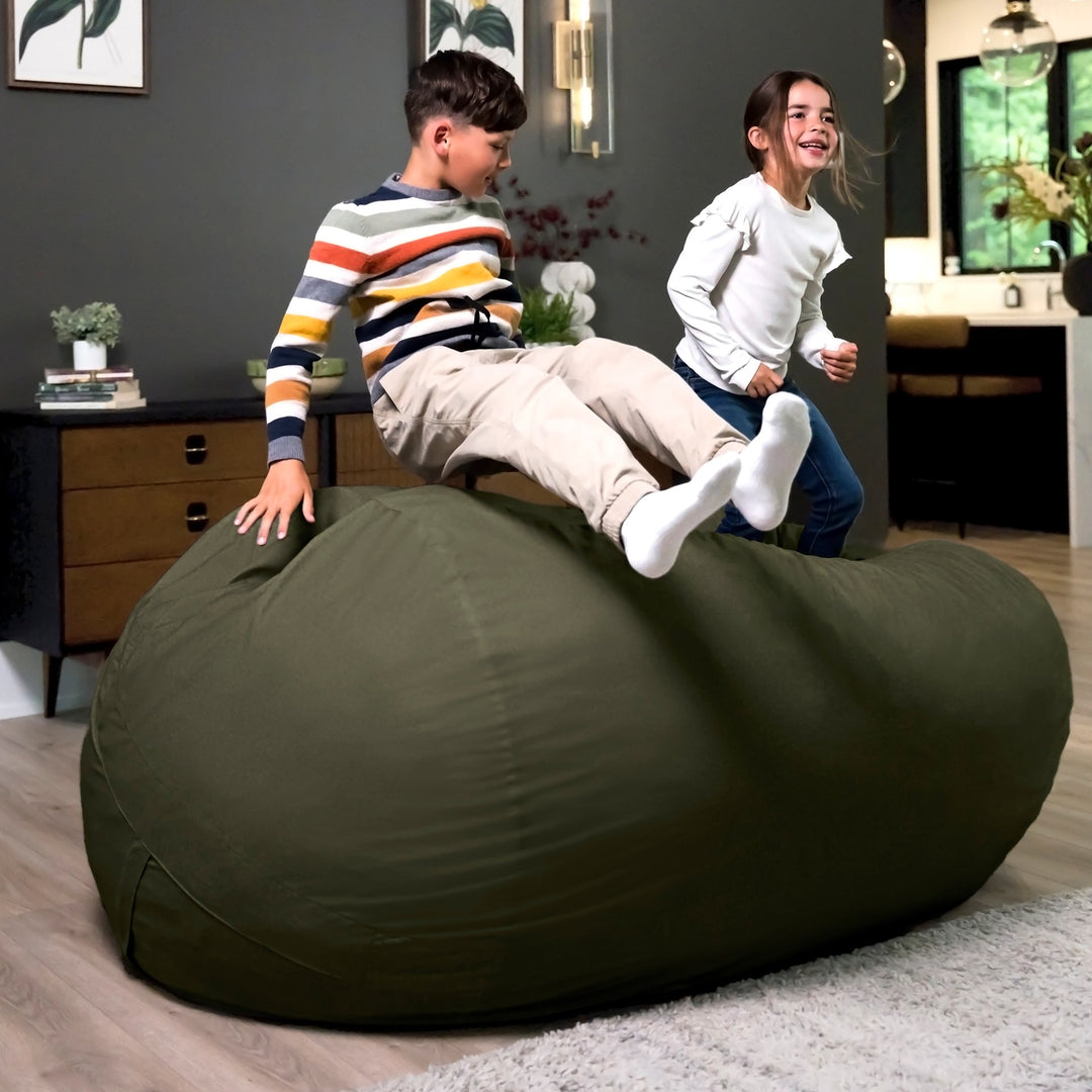 Two children playing on a large green bean bag in a room with a desk and plants. #color_forest-green-velveteen