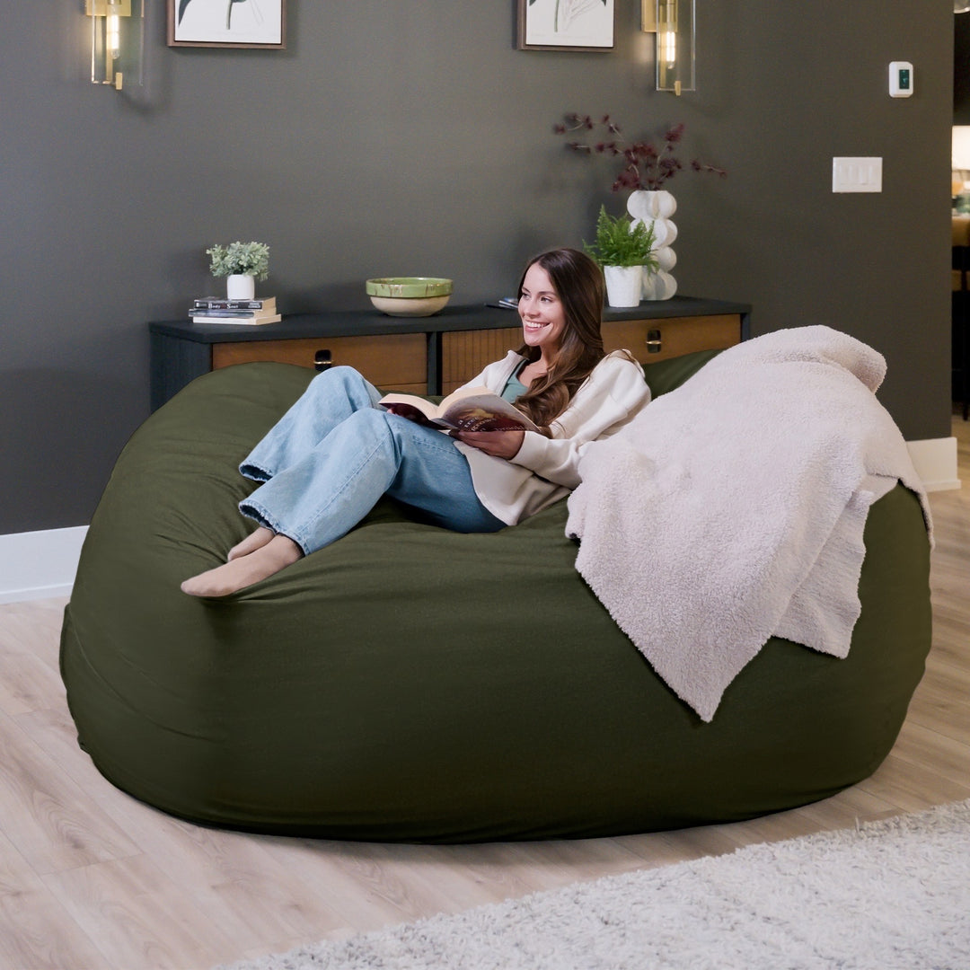 Woman relaxing on a large green bean bag chair in a cozy living room. #color_forest-green-velveteen