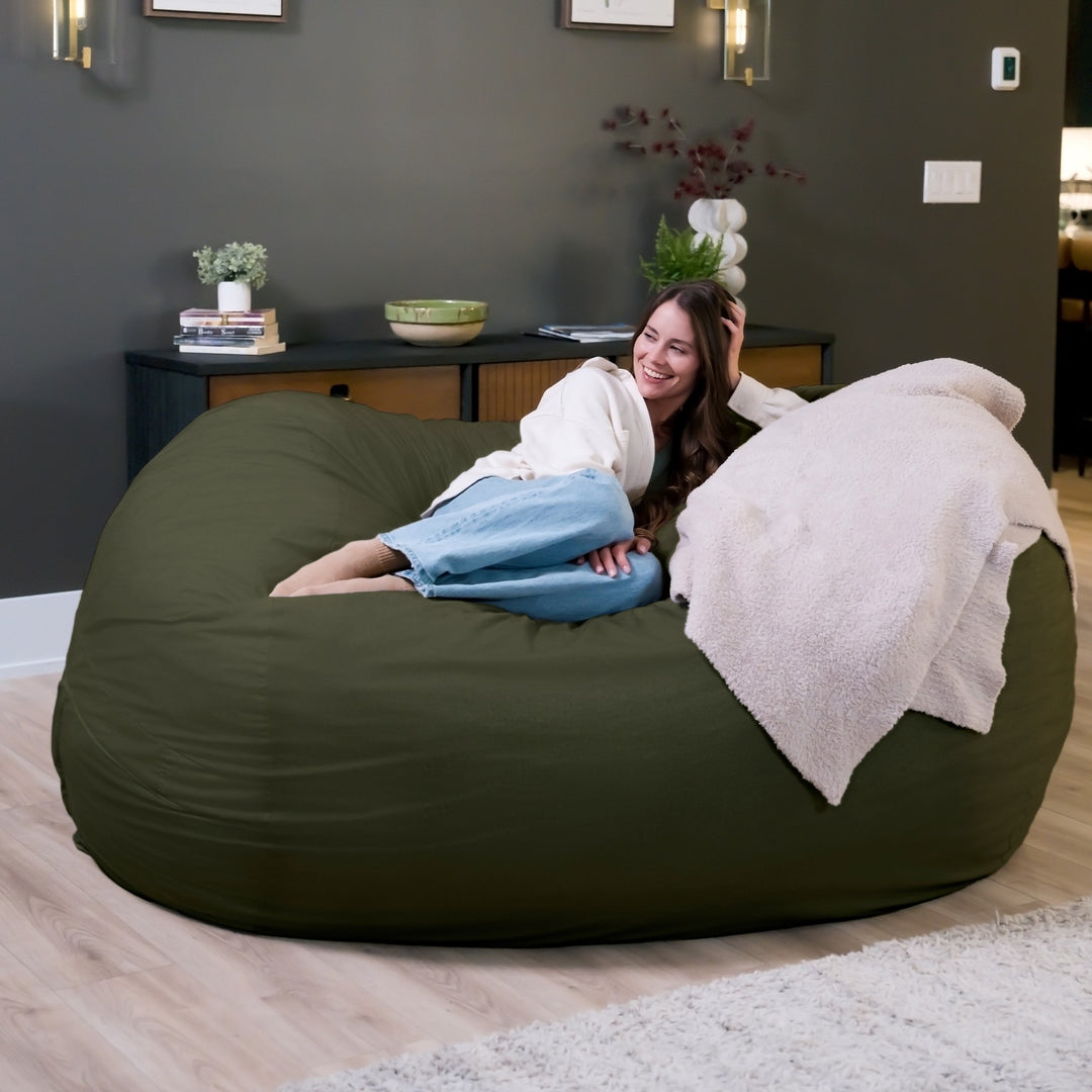 Woman sitting on a large green bean bag in a room with a dark gray wall and wooden floor. #color_forest-green-velveteen