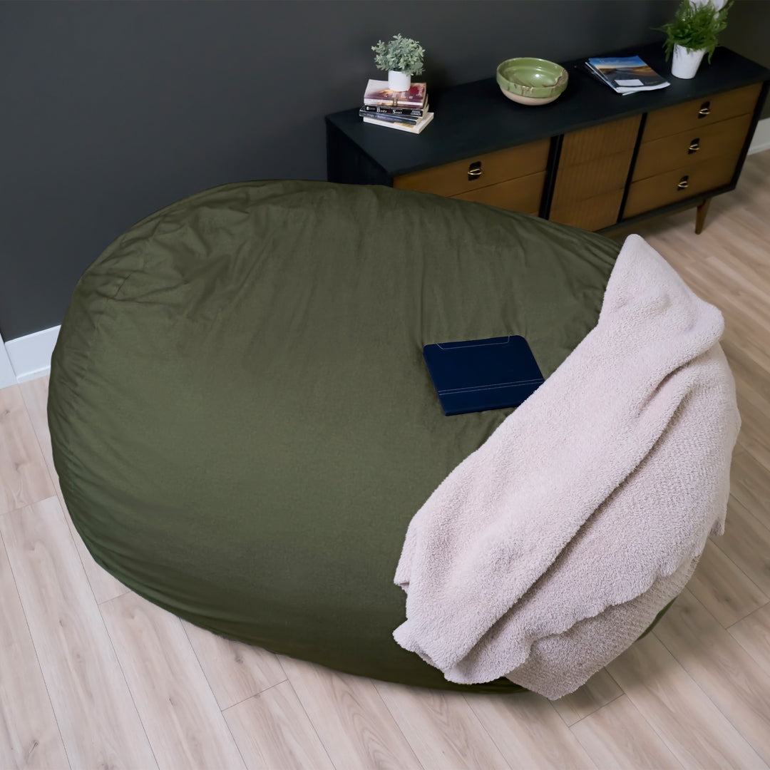 Large green bean bag chair with a pink blanket on a wooden floor. #color_forest-green-velveteen