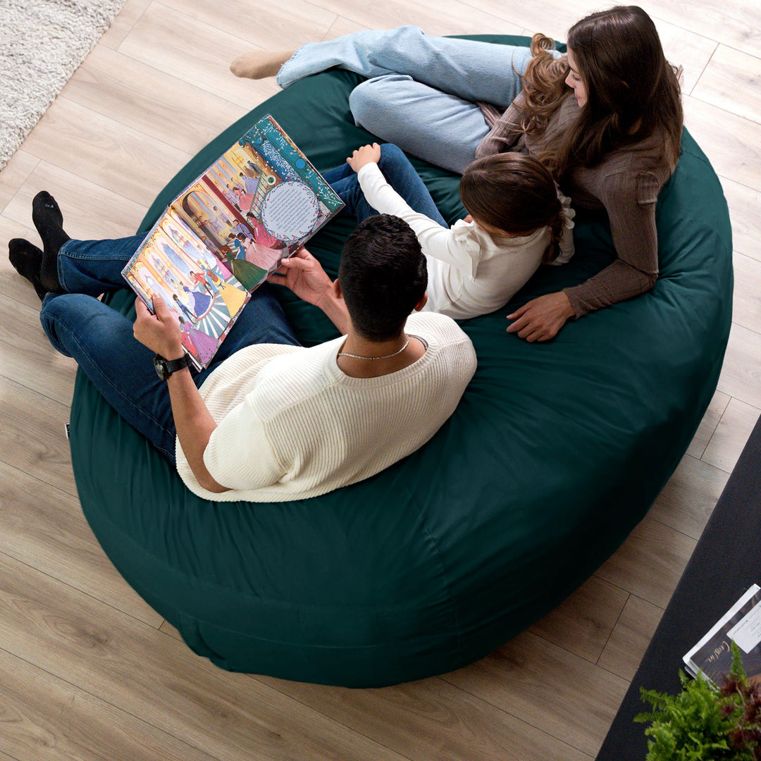 Family sitting on a large green bean bag reading a book together. #color_deep-sea-velveteen