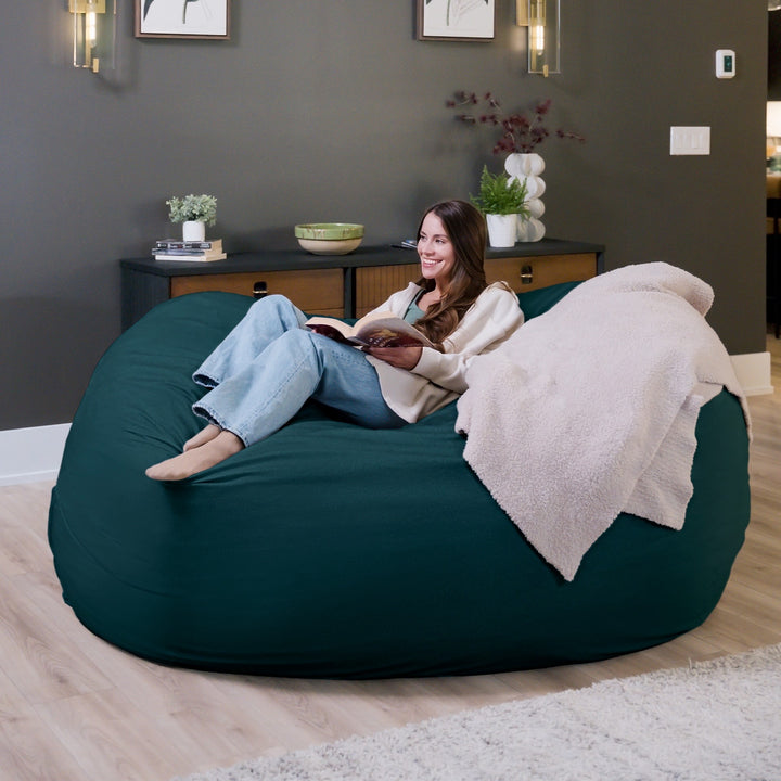 Woman reading a book on a large green bean bag chair in a cozy living room. #color_deep-sea-velveteen