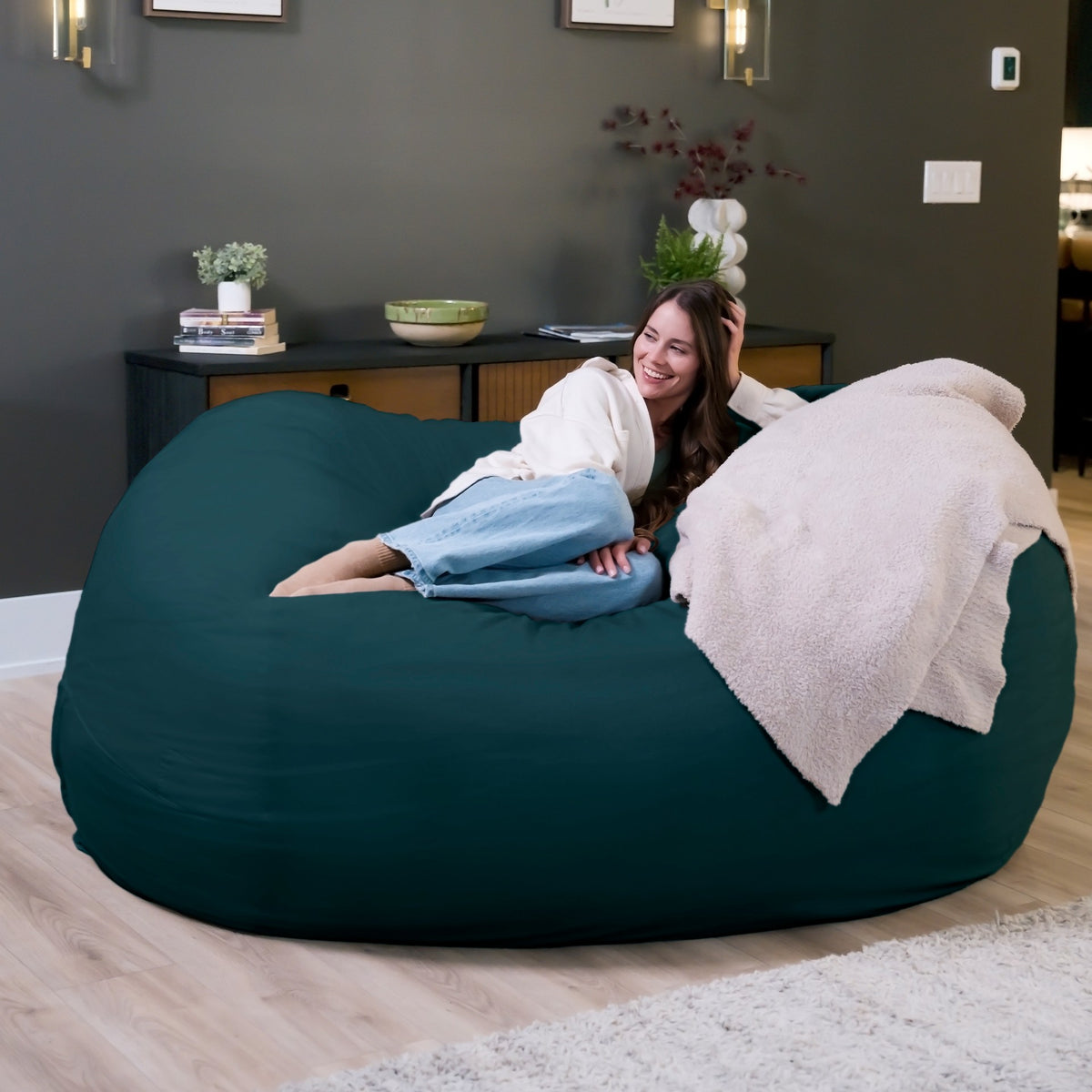 Woman relaxing on a large teal bean bag chair in a cozy living room. 
