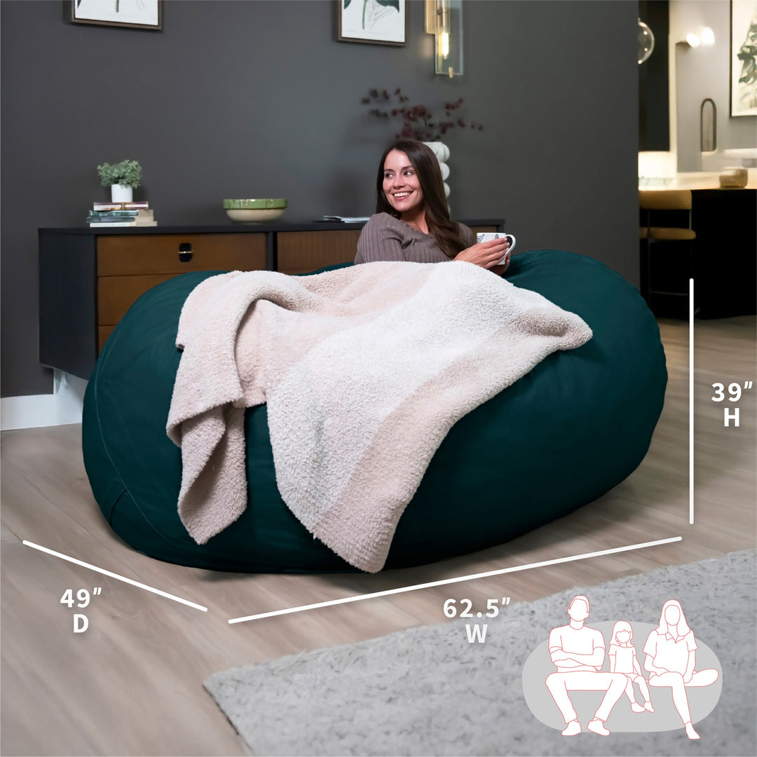 Woman sitting on a large teal bean bag with dimensions displayed #color_deep-sea-velveteen