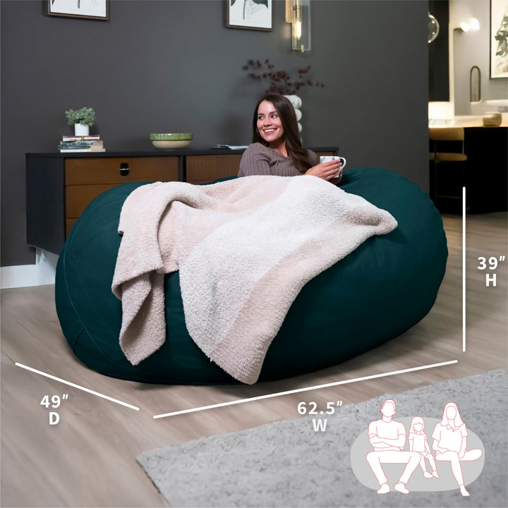 Woman sitting on a large teal bean bag with dimensions displayed #color_deep-sea-velveteen