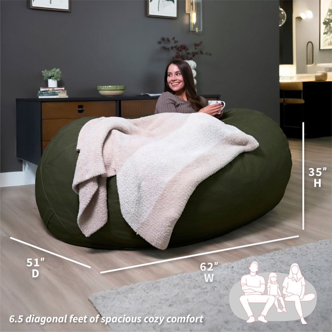 Woman sitting on a large green bean bag with a blanket, surrounded by room dimensions and usage illustrations. #color_forest-green-velveteen