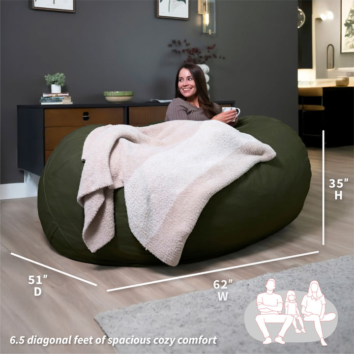 Woman sitting on a large green bean bag with a blanket, surrounded by room dimensions and usage illustrations. #color_forest-green-velveteen