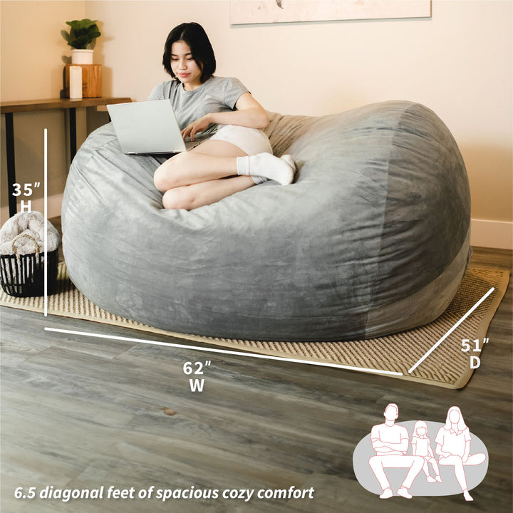 Woman sitting on a large gray bean bag chair with measurements indicated #color_gray-plush