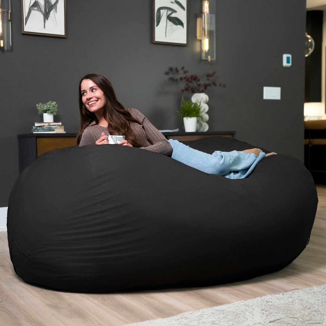 Woman sitting on a large black bean bag in a modern living room. #color_black-brushed-denim
