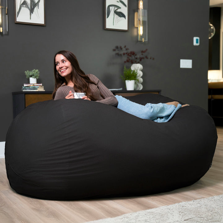 Woman sitting on a large black bean bag in a modern living room. #color_black-brushed-denim