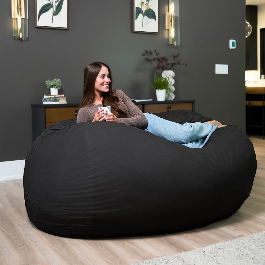 Woman sitting on a large black bean bag chair in a modern living room. #color_black-brushed-denim