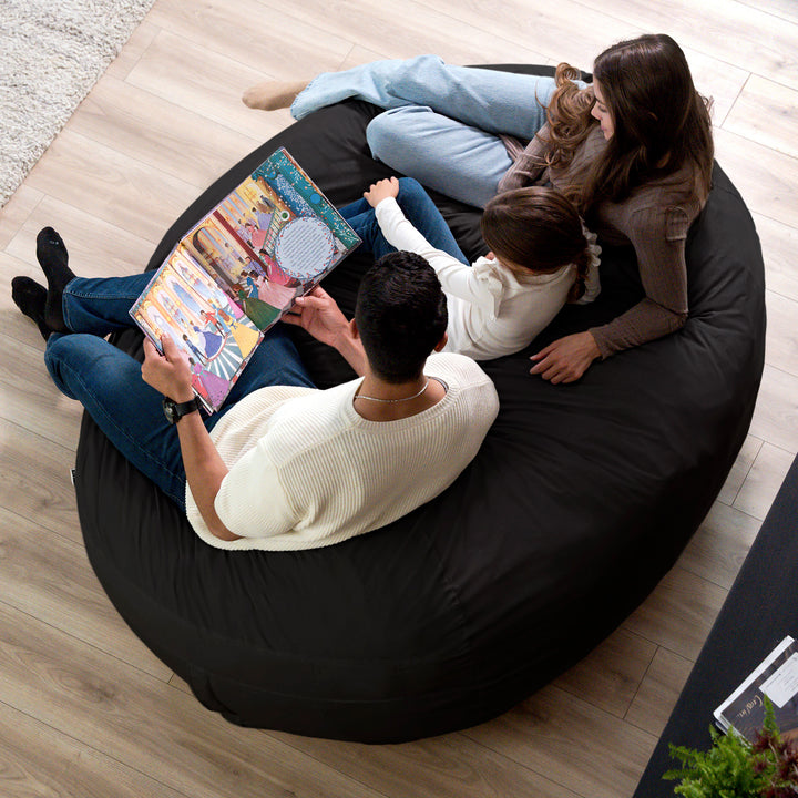 Family sitting on a bean bag reading a book together #color_black-brushed-denim