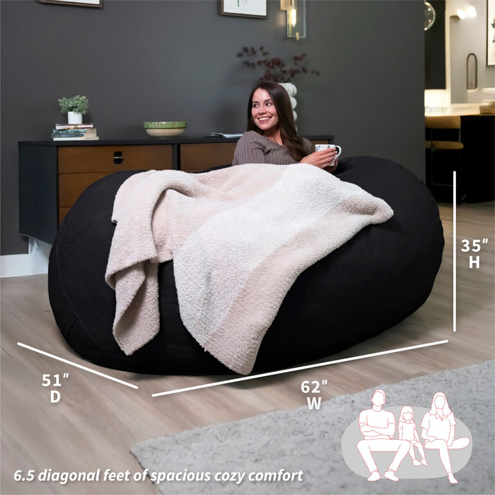 Woman sitting on a large black bean bag with dimensions displayed, in a room setting. #color_black-brushed-denim