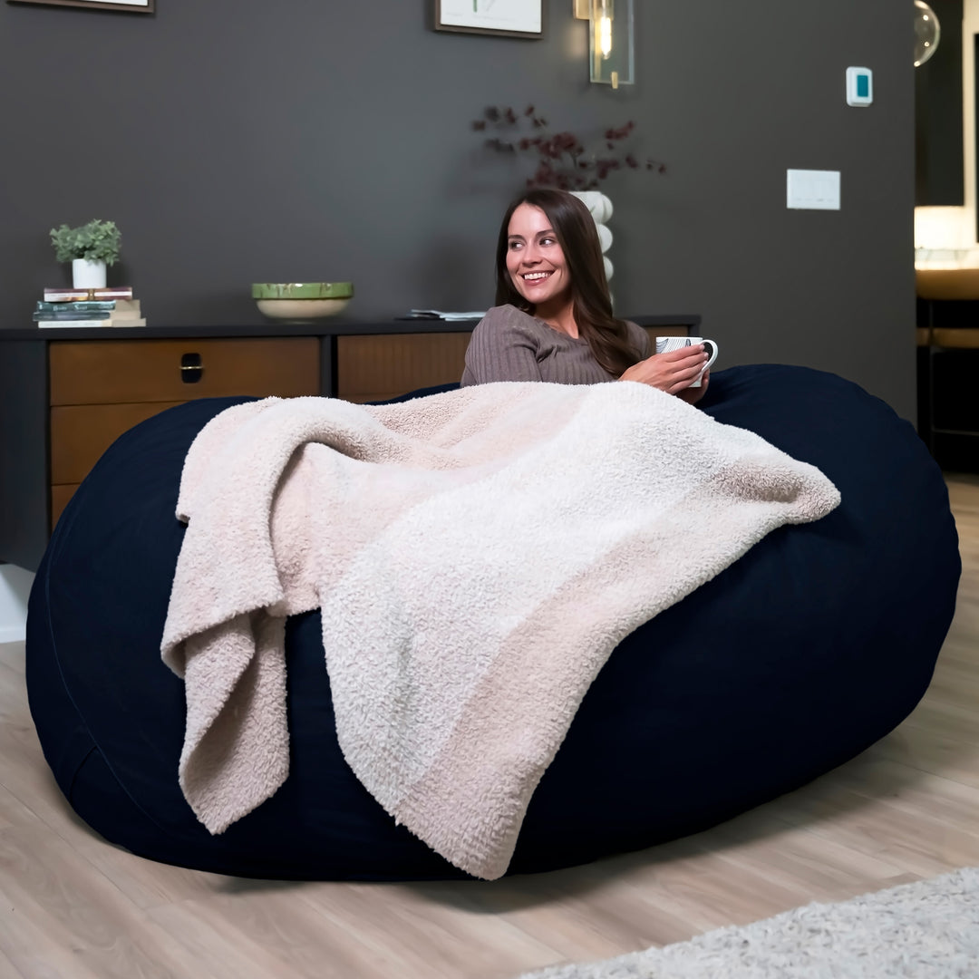 Woman sitting on a large bean bag with a blanket, holding a mug in a room. #color_cobalt-brushed-denim