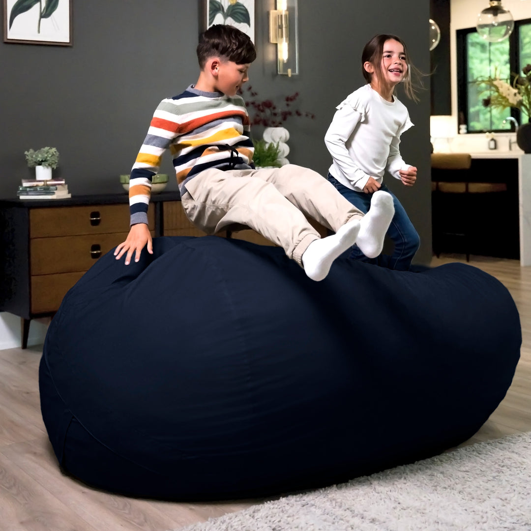 Two children playing on a large navy bean bag in a room with a desk and plants. #color_cobalt-brushed-denim