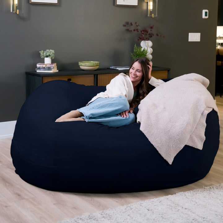 Woman lounging on a large navy bean bag chair in a cozy living room. #color_cobalt-brushed-denim