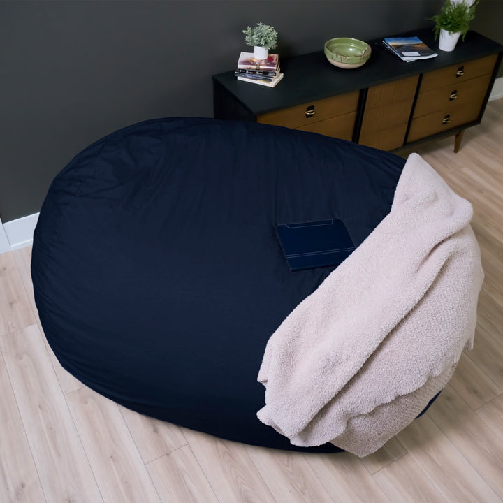 Large dark blue bean bag chair with a beige blanket on a wooden floor. #color_cobalt-brushed-denim