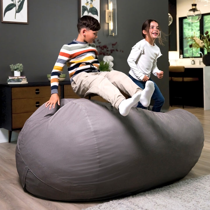Two children playing on a large gray bean bag in a room with a dark wall and furniture. #color_fog-brushed-denim