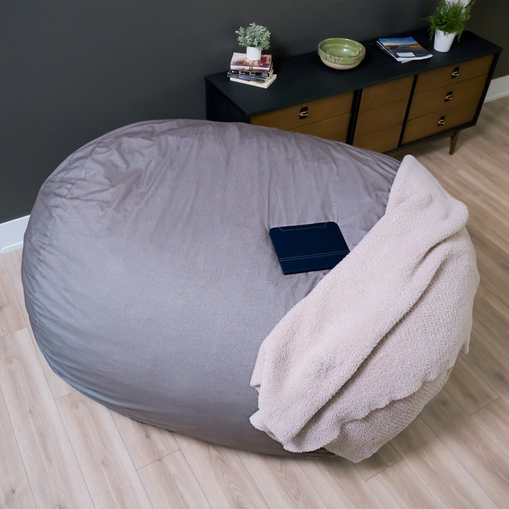 Gray bean bag chair with a blanket on a wooden floor in a room with a dresser and plants. #color_fog-brushed-denim